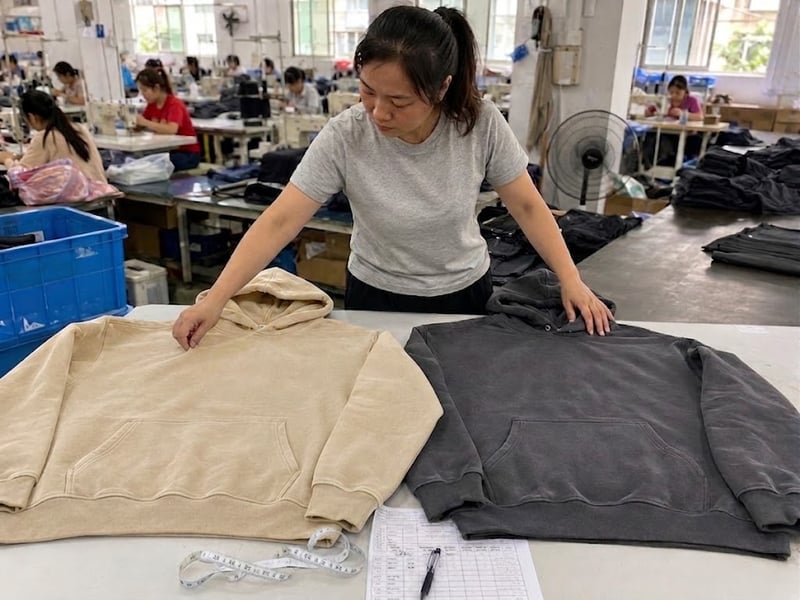 Female QC inspector comparing bulk heavyweight hoodies with the approved production sample
